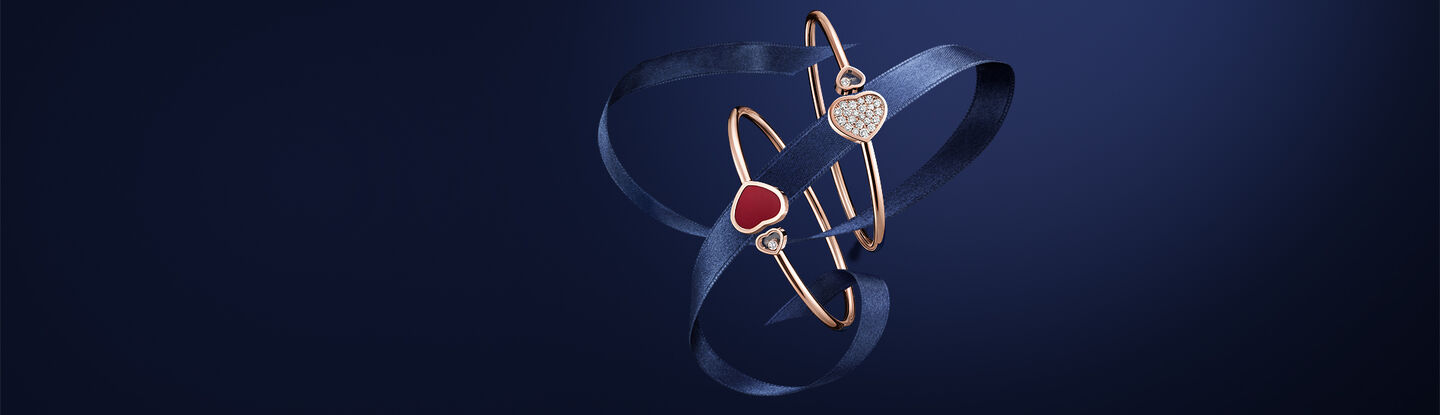 Chopard Happy Hearts rose gold bangles with diamond and red heart motifs wrapped in a navy satin ribbon